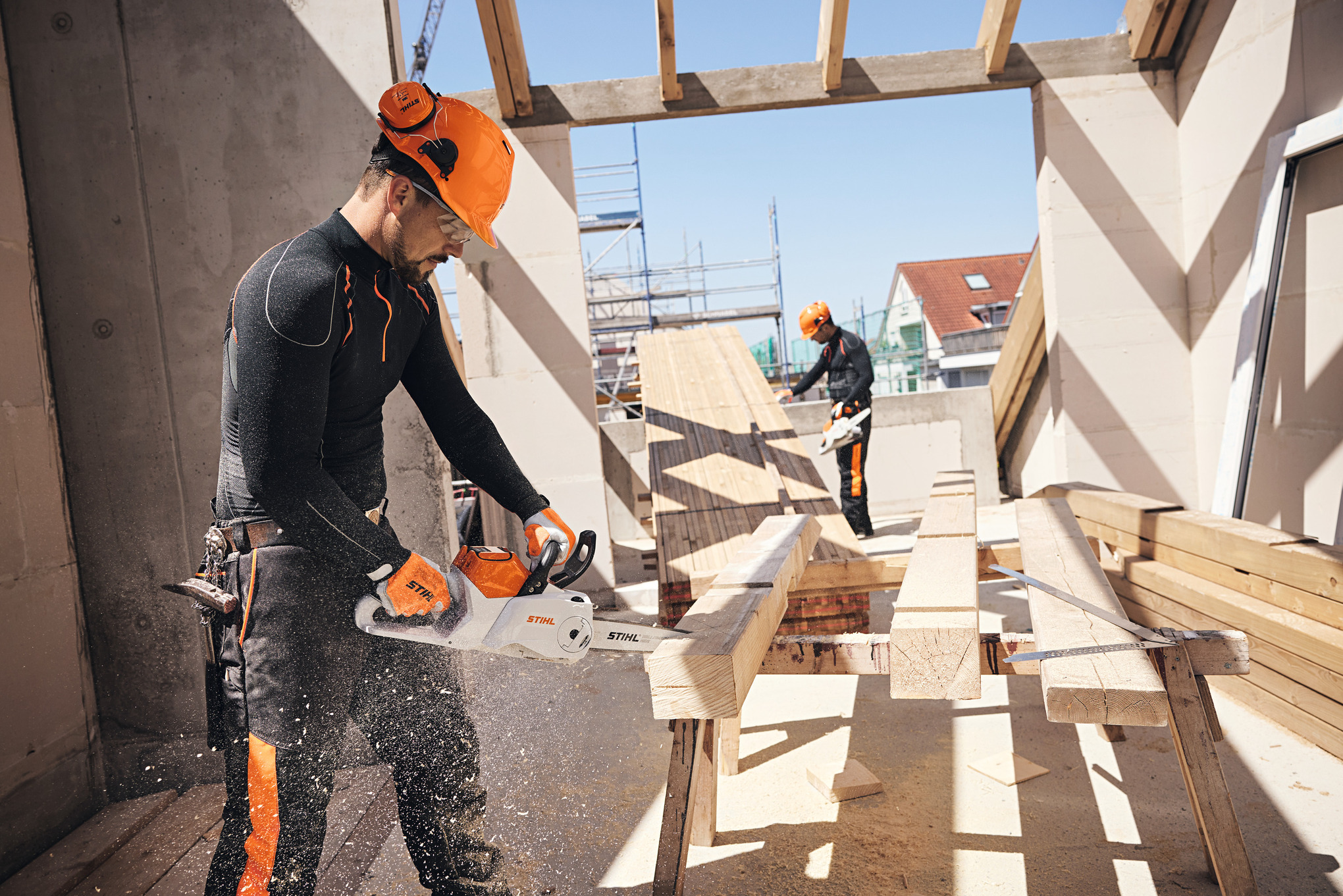 A person in personal protective equipment sawing a wooden plank.