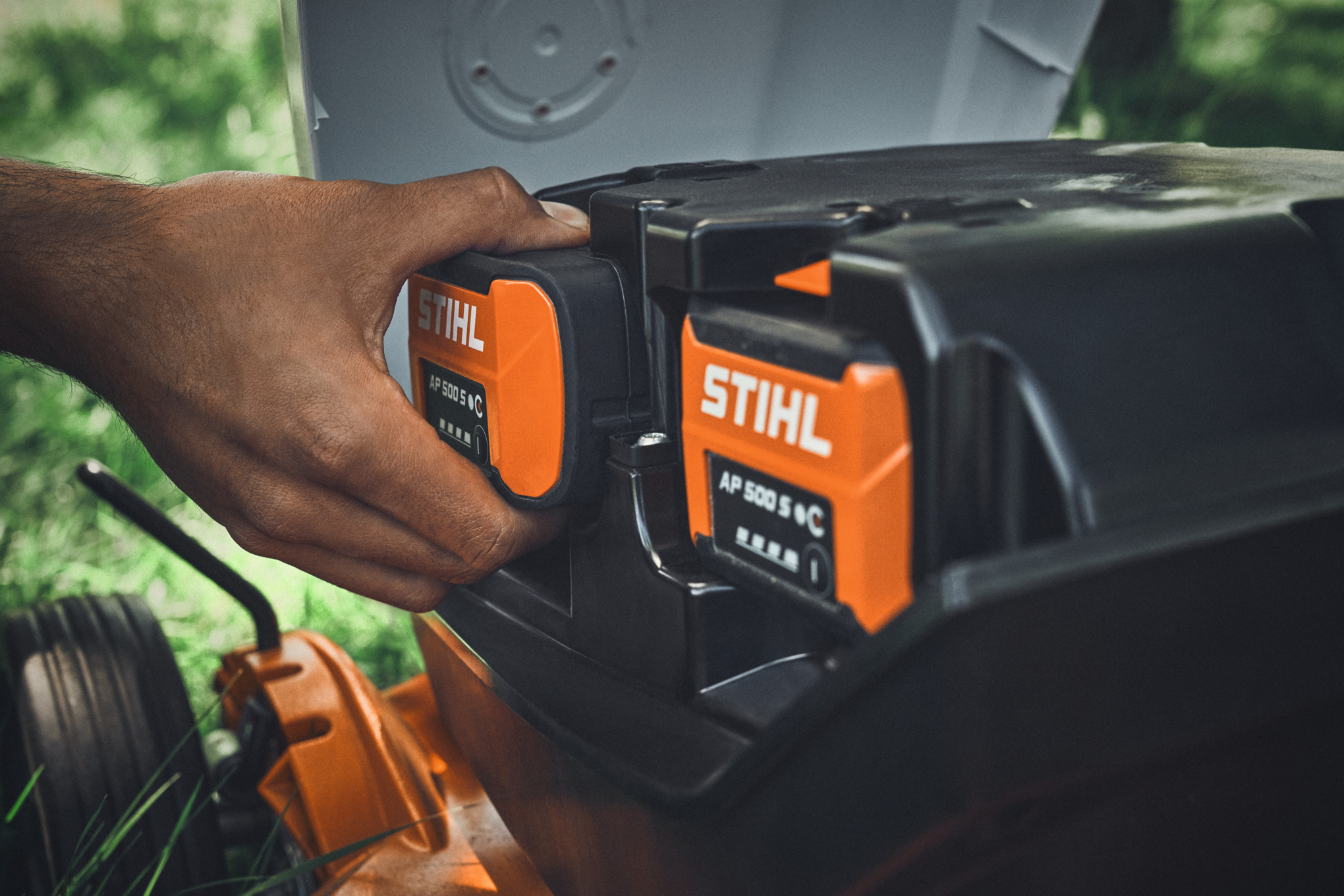 A person inserting a STIHL AP 500 S battery into a STIHL battery-powered lawn mower