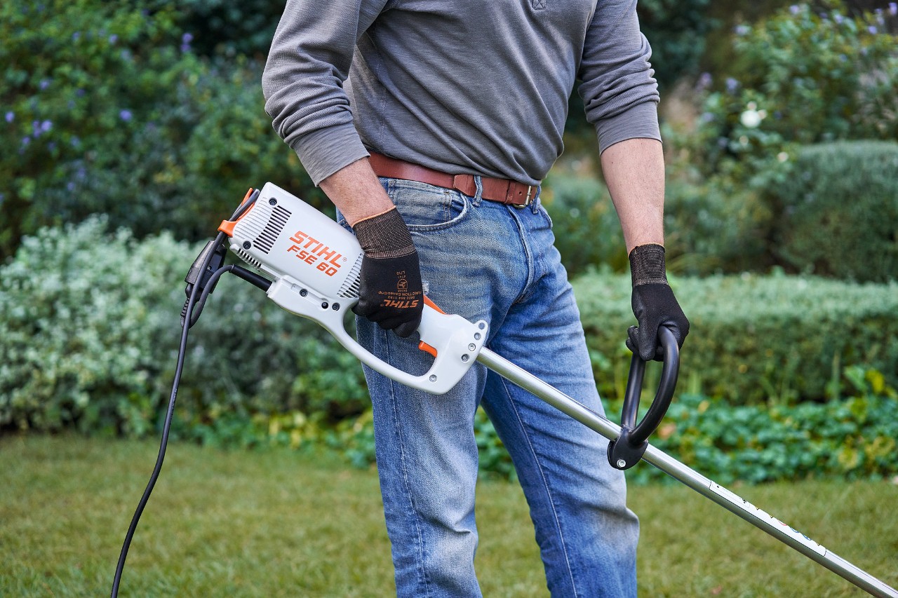 A man wearing protective gloves holding a STIHL FSE 60 electric brushcutter with both hands